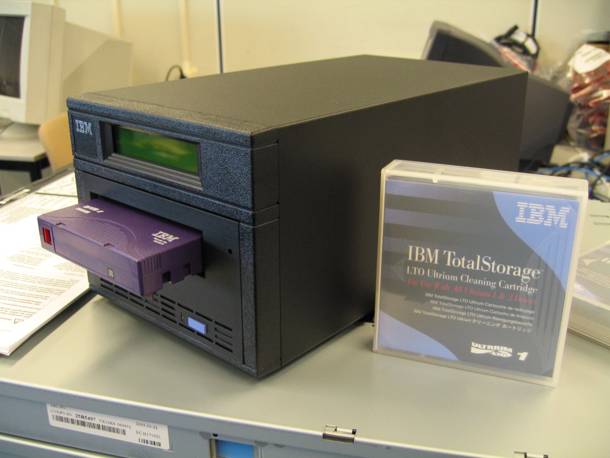 黒いテープ装置に紫色のカートリッジが差し込まれ、その横にIBMのクリーニング用カートリッジが置かれている